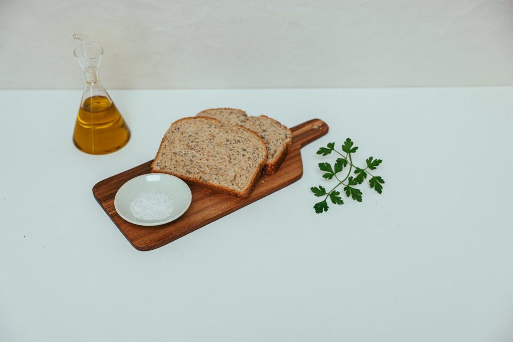 A minimalist still life of wheat bread, olive oil, and parsley on a wooden board.